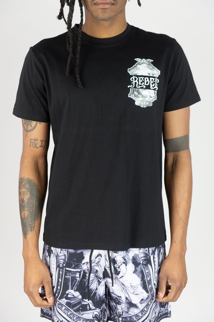 Person wearing a black t-shirt with a graphic design and patterned shorts on a white background