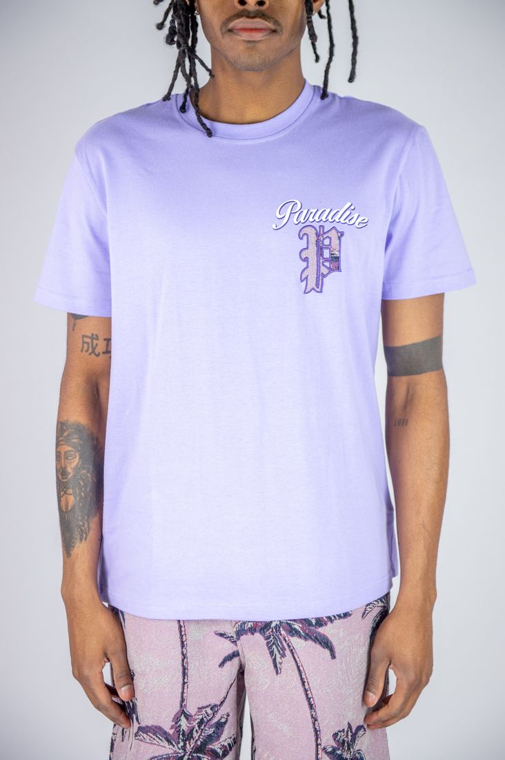 Person wearing a light purple t-shirt with a logo and text, standing against a plain background