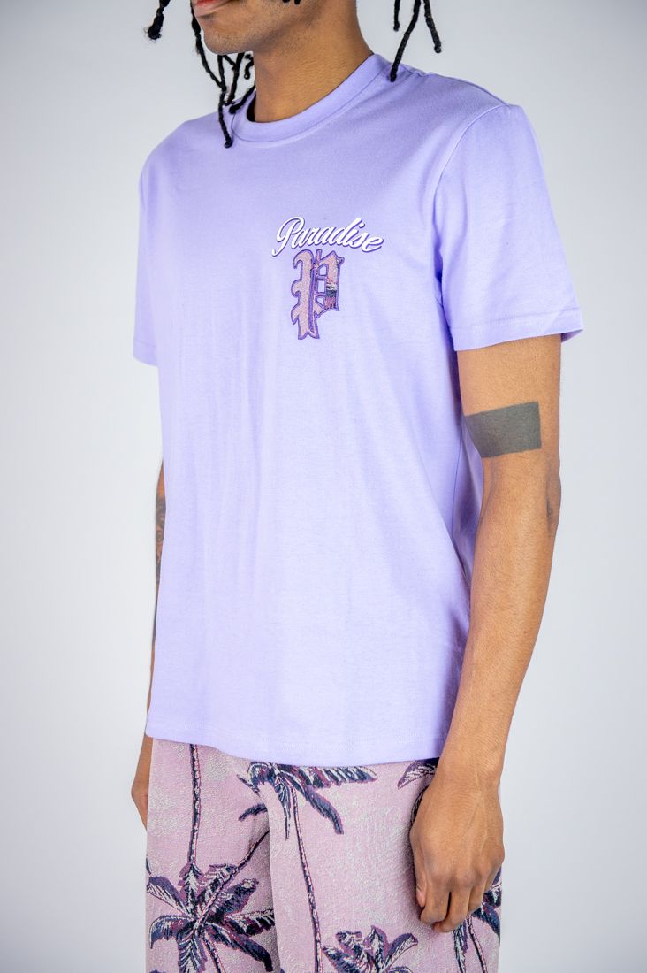 Person wearing a light purple t-shirt with a logo and text, standing against a plain background.