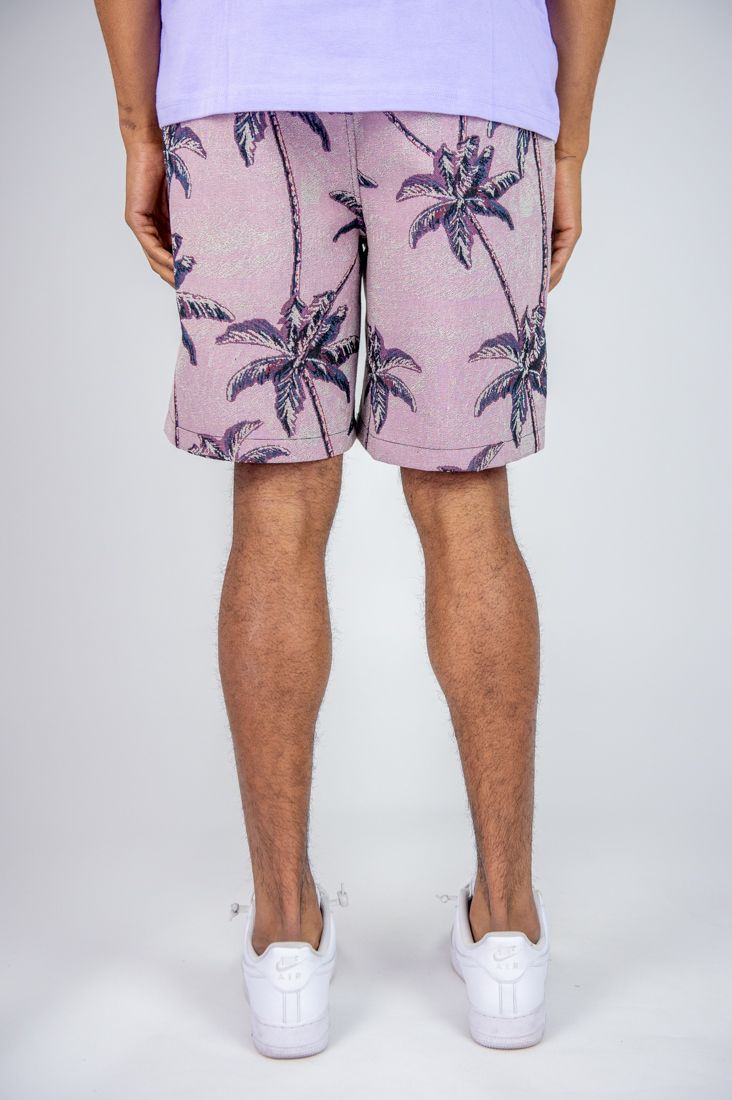 Person wearing pink shorts with palm tree pattern on a white background