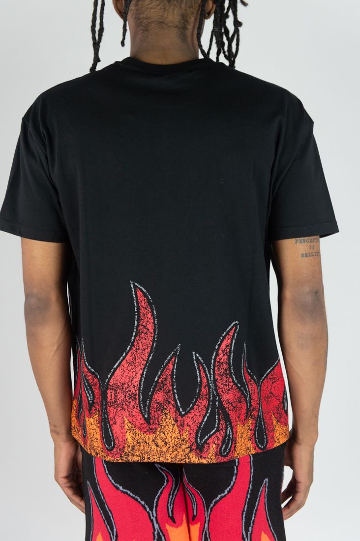 Person wearing a black t-shirt with flame design on the back, standing against a plain background.