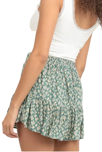 Woman wearing a white tank top and green floral skirt on a plain background