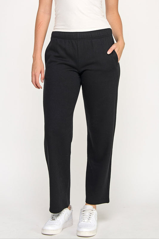 Woman wearing a white tank top and black pants on a plain background