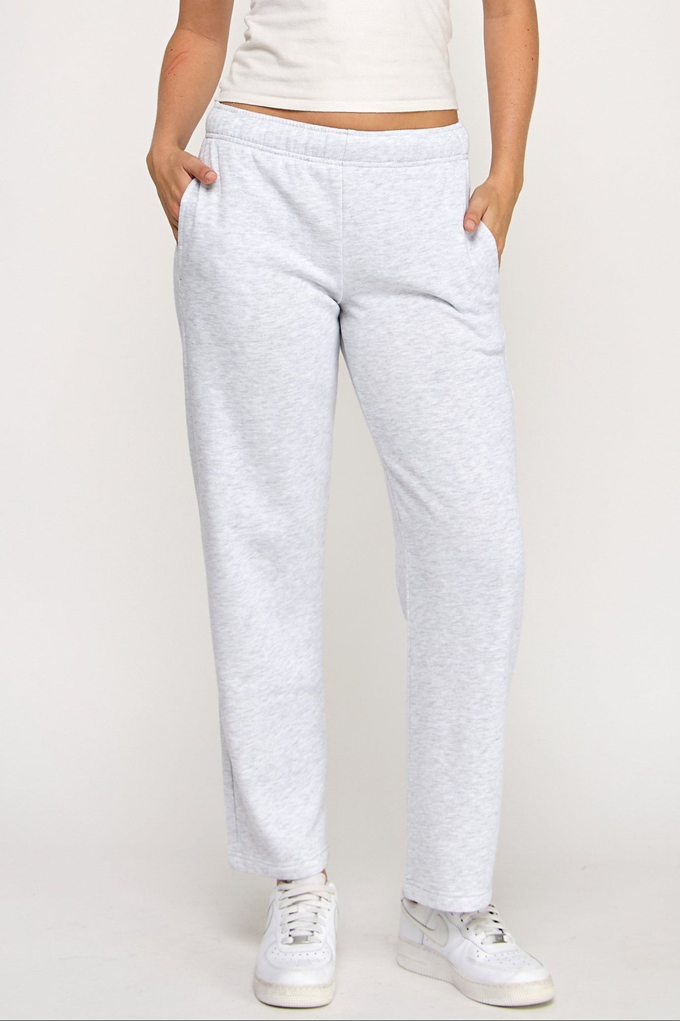 Woman wearing a white tank top and light gray sweatpants on a plain background