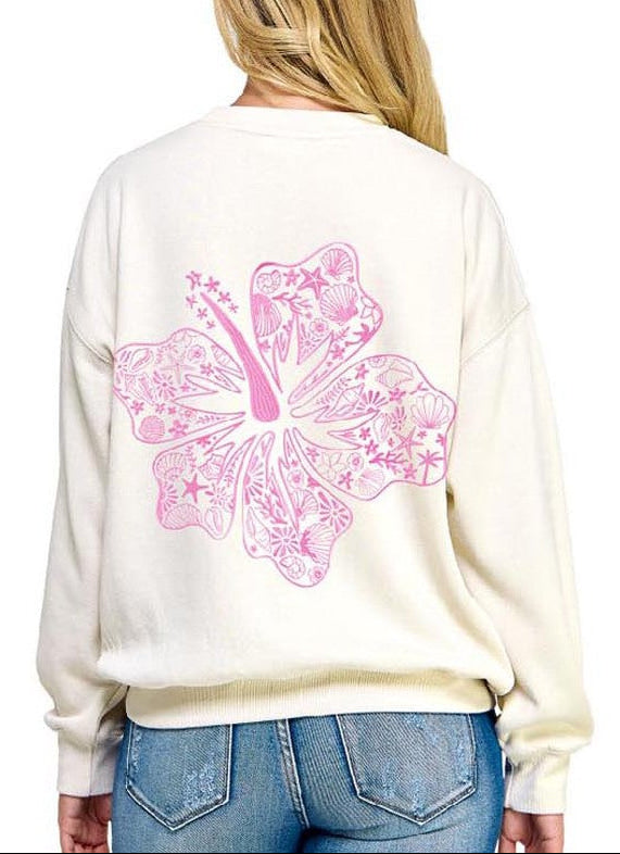 Woman wearing a cream sweatshirt with a pink butterfly design on the back, standing against a white background.