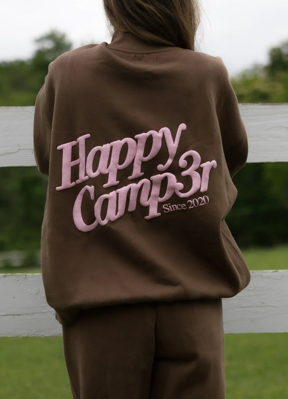 Person wearing a brown sweatshirt with 'Happy Camp3r Since 2020' text outdoors.
