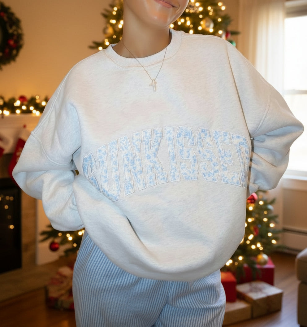Person wearing a light blue sweatshirt with text, sitting on a couch.