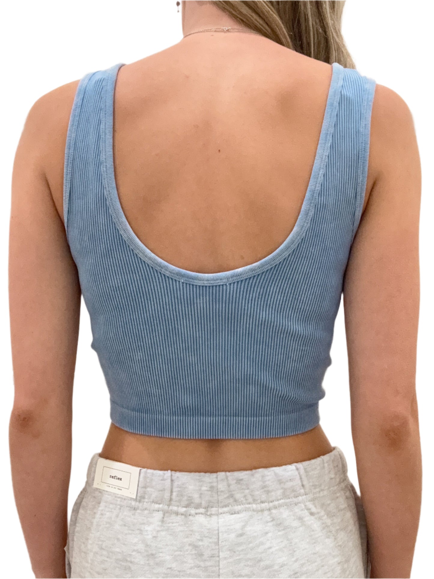 Person wearing a blue ribbed crop top and gray sweatpants in a neutral setting