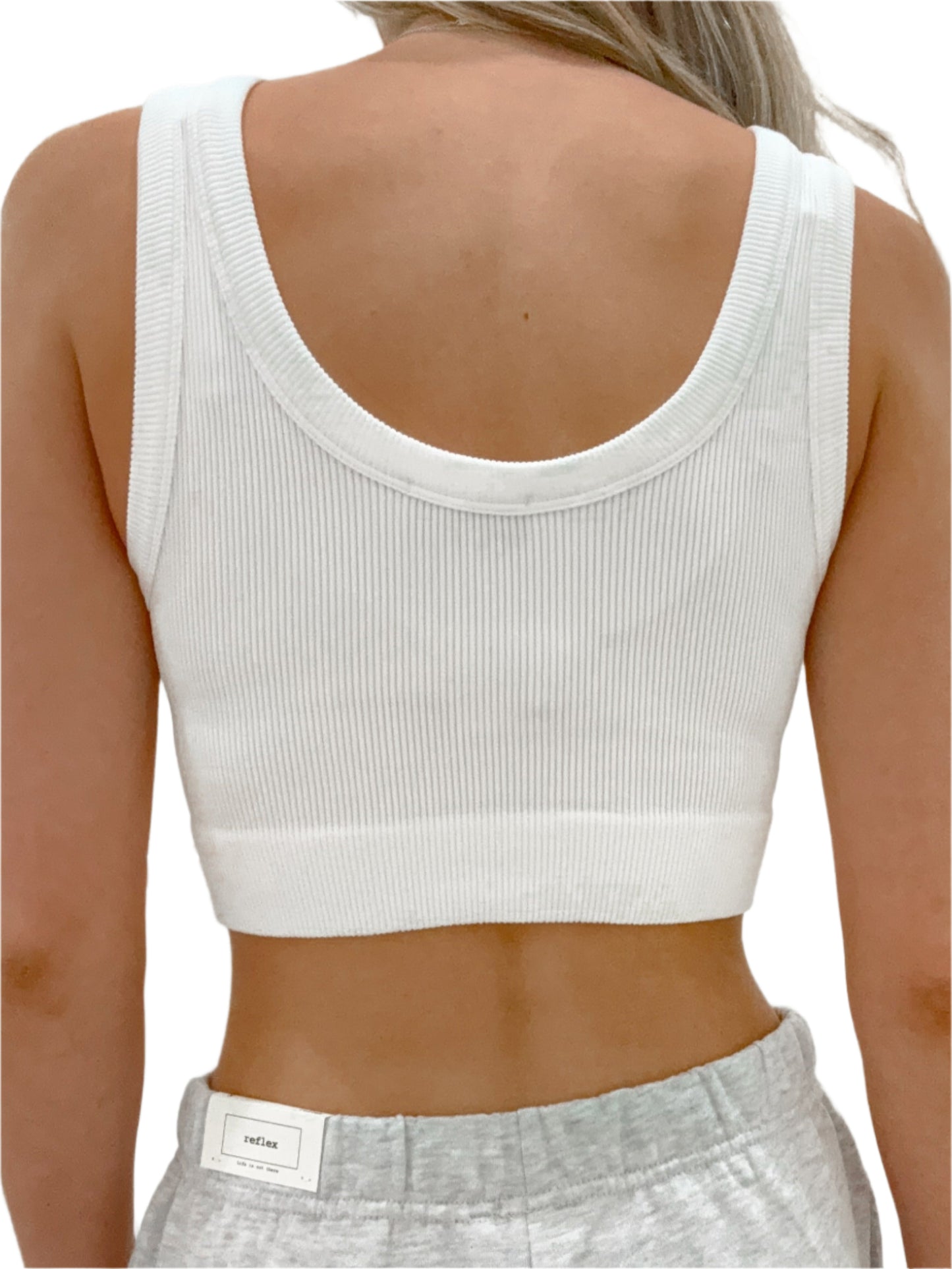 Person wearing a white ribbed tank top and gray sweatpants against a light background