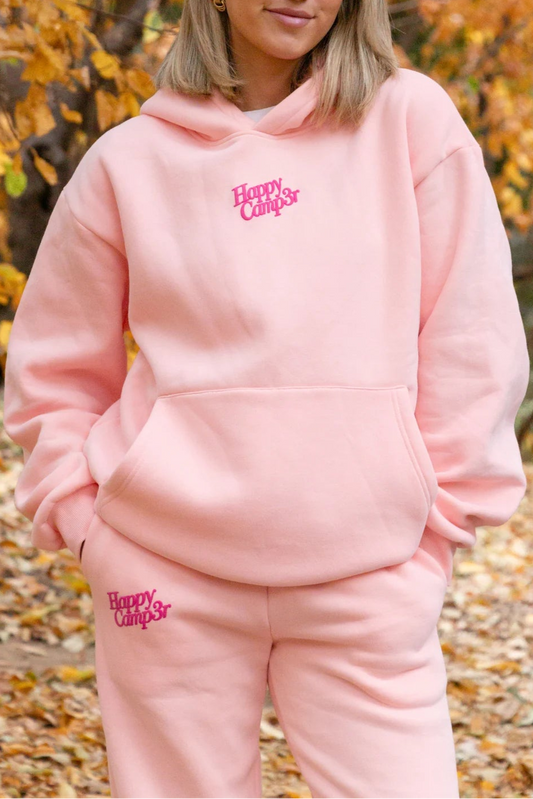 Person wearing a pink 'Happy Campers' hoodie and pants in an autumn setting.