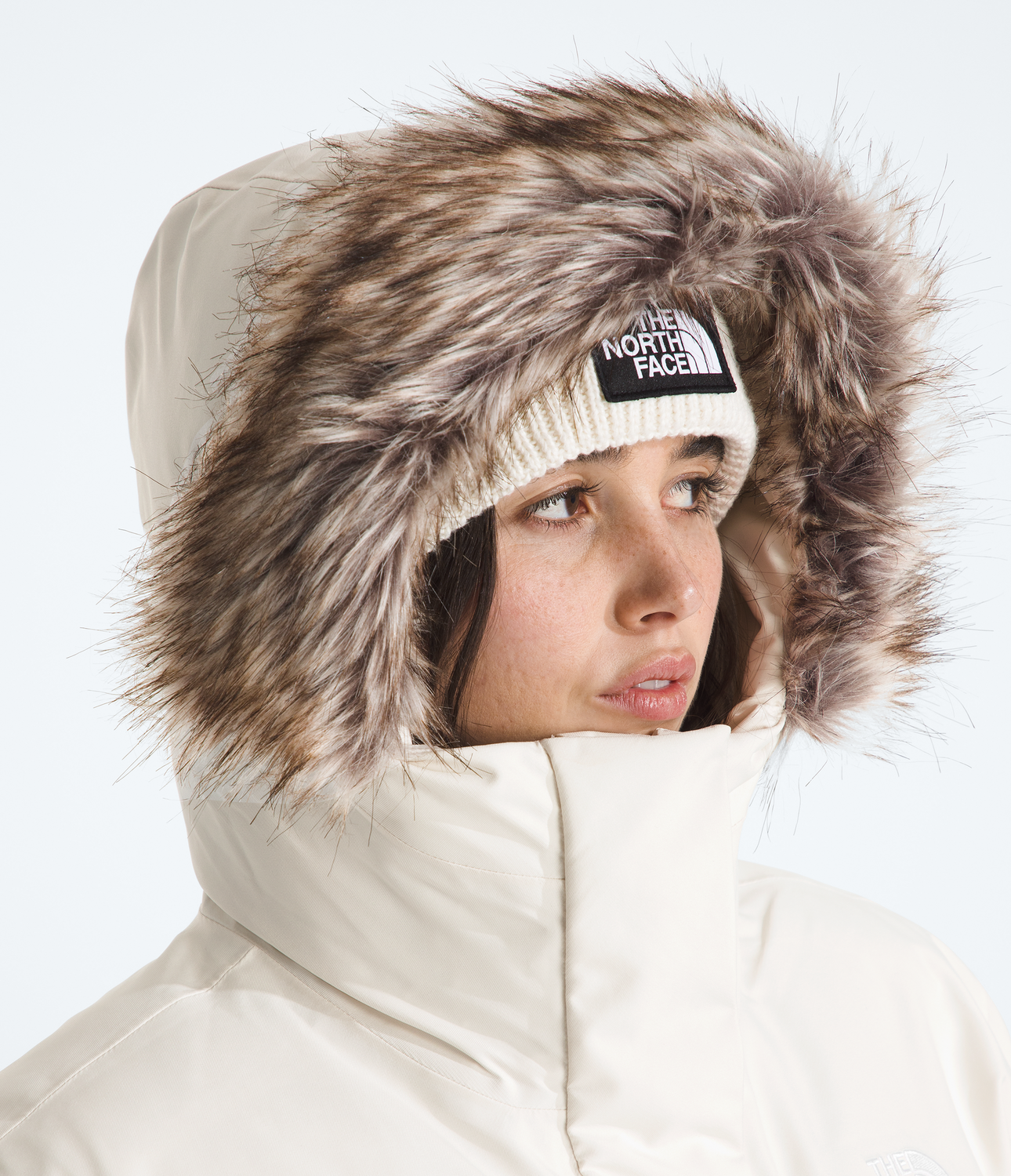 Person wearing a white winter coat with a fur-lined hood and The North Face beanie.