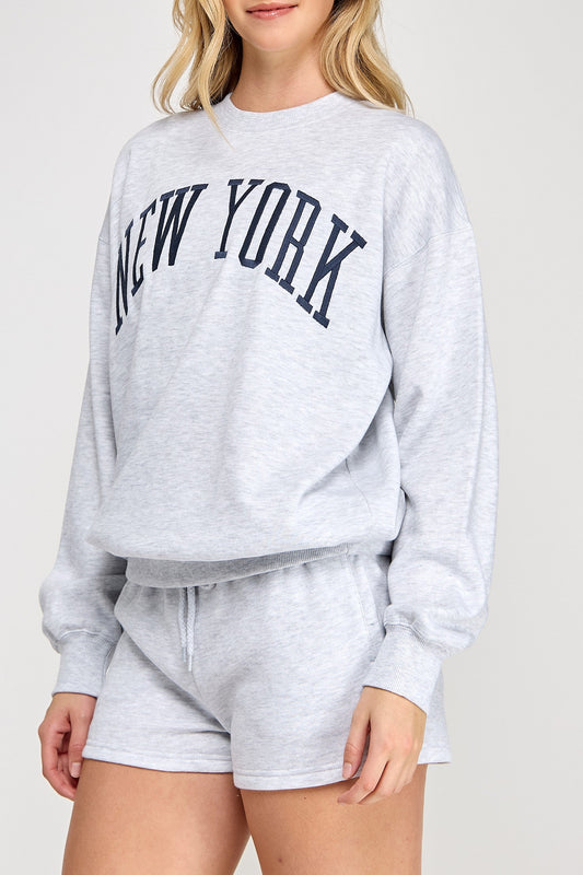 Woman wearing a gray 'New York' sweatshirt and shorts on a white background