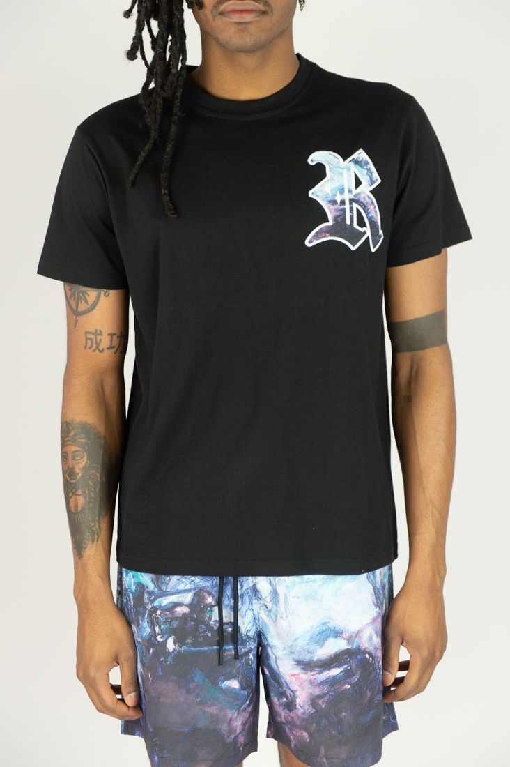 Person wearing a black t-shirt with a logo and colorful shorts on a white background