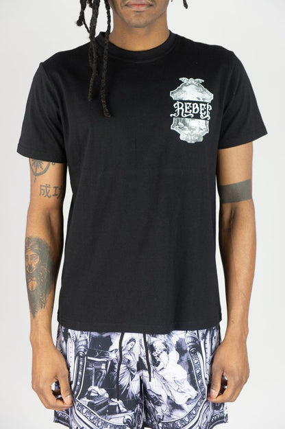 Person wearing a black t-shirt with a graphic design and patterned shorts on a white background