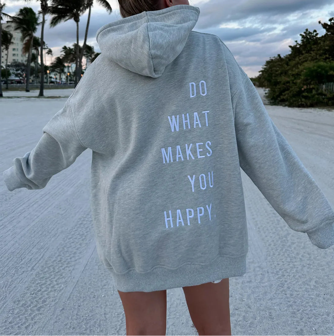 Person wearing a gray hoodie with 'Do What Makes You Happy' text on a beach.