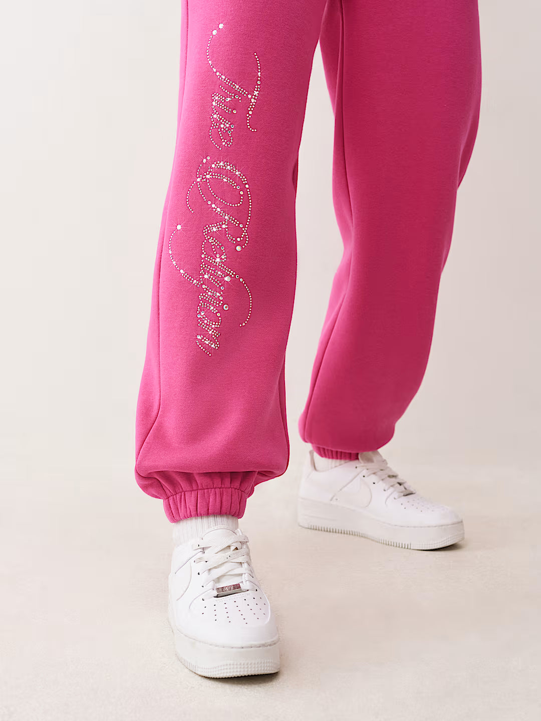 Pink sweatpants with white text and white sneakers on a light background