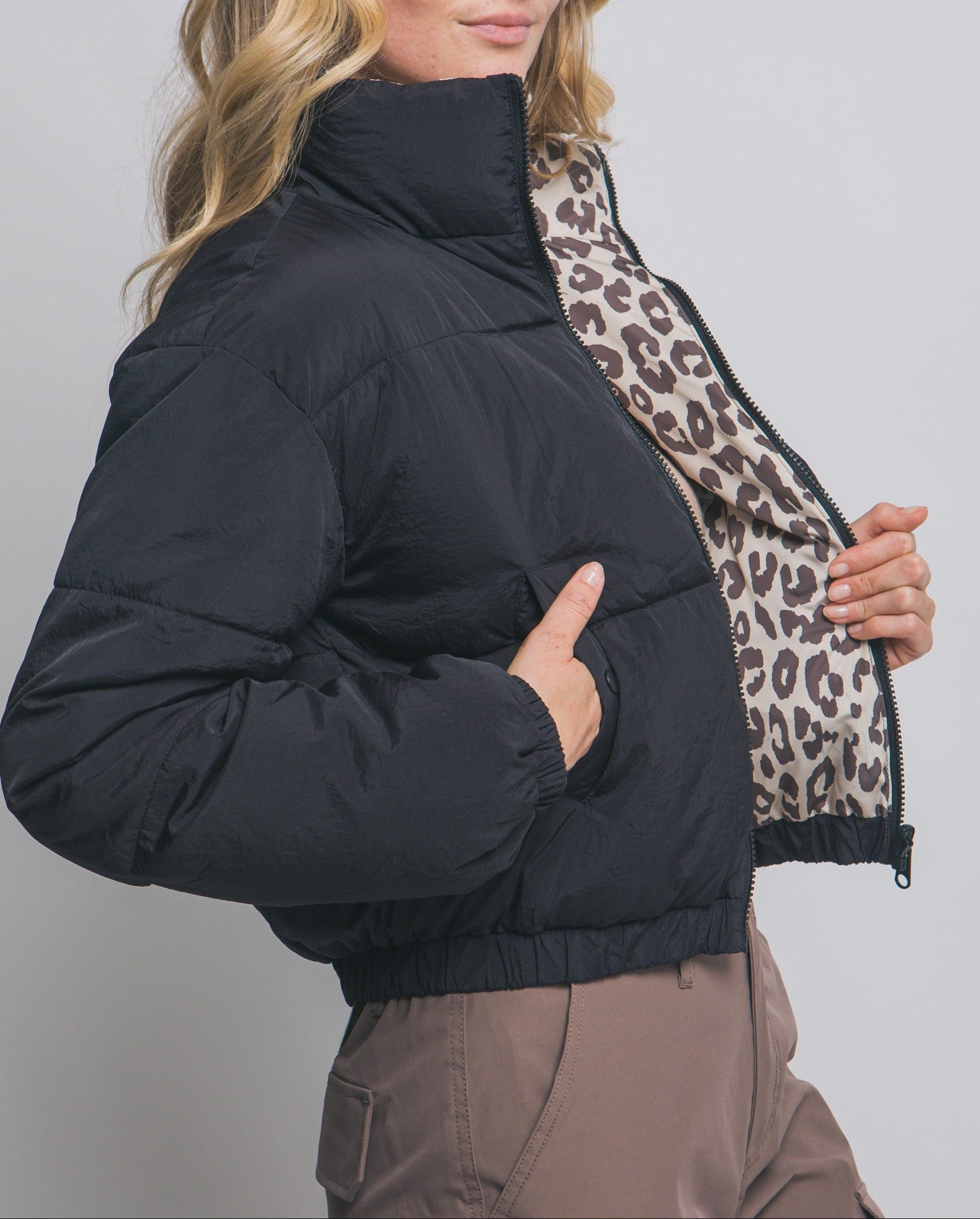 Woman wearing a black puffer jacket with a leopard print scarf against a plain background