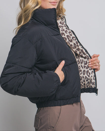 Woman wearing a black puffer jacket with a leopard print scarf against a plain background