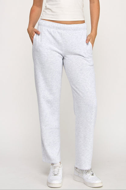 Woman wearing a white tank top and light gray sweatpants on a plain background