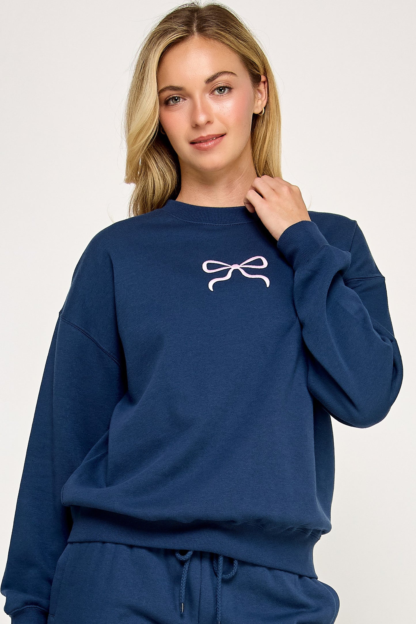 Person wearing a blue sweatshirt with a white bow design on a plain background