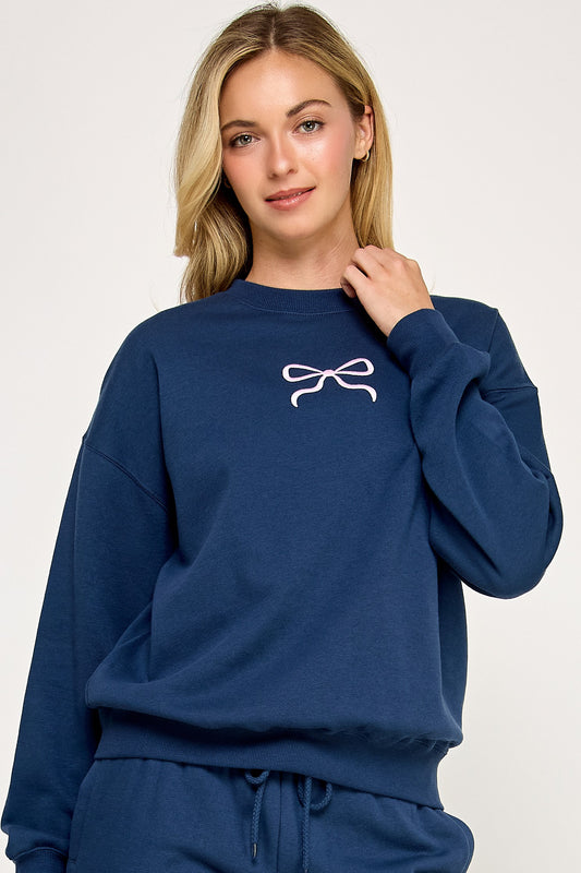 Person wearing a blue sweatshirt with a white bow design on a plain background