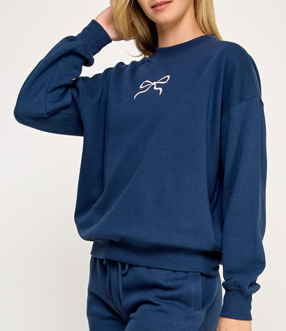 Woman wearing a navy blue sweatshirt and shorts set with a logo on a white background. 