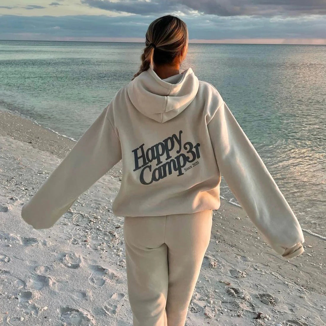 Person wearing a 'Happy Camp31' hoodie on a beach