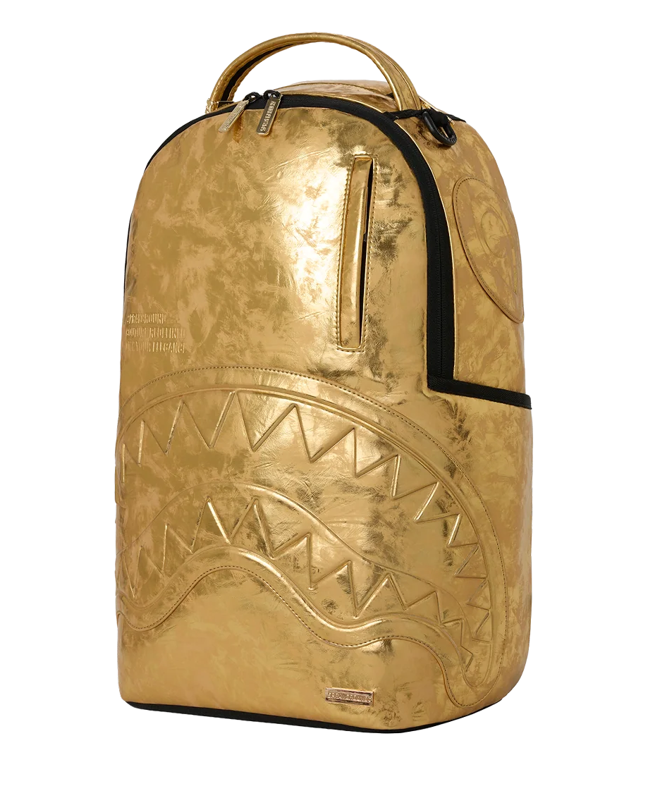 A metallic gold spray backpack with a shark face design embossed on the front, black zipper accents, and a top handle, shown against a plain white background.