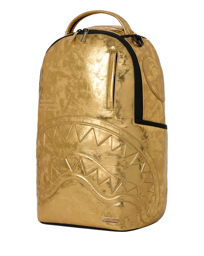 A metallic gold spray backpack with a shark face design embossed on the front, black zipper accents, and a top handle, shown against a plain white background.