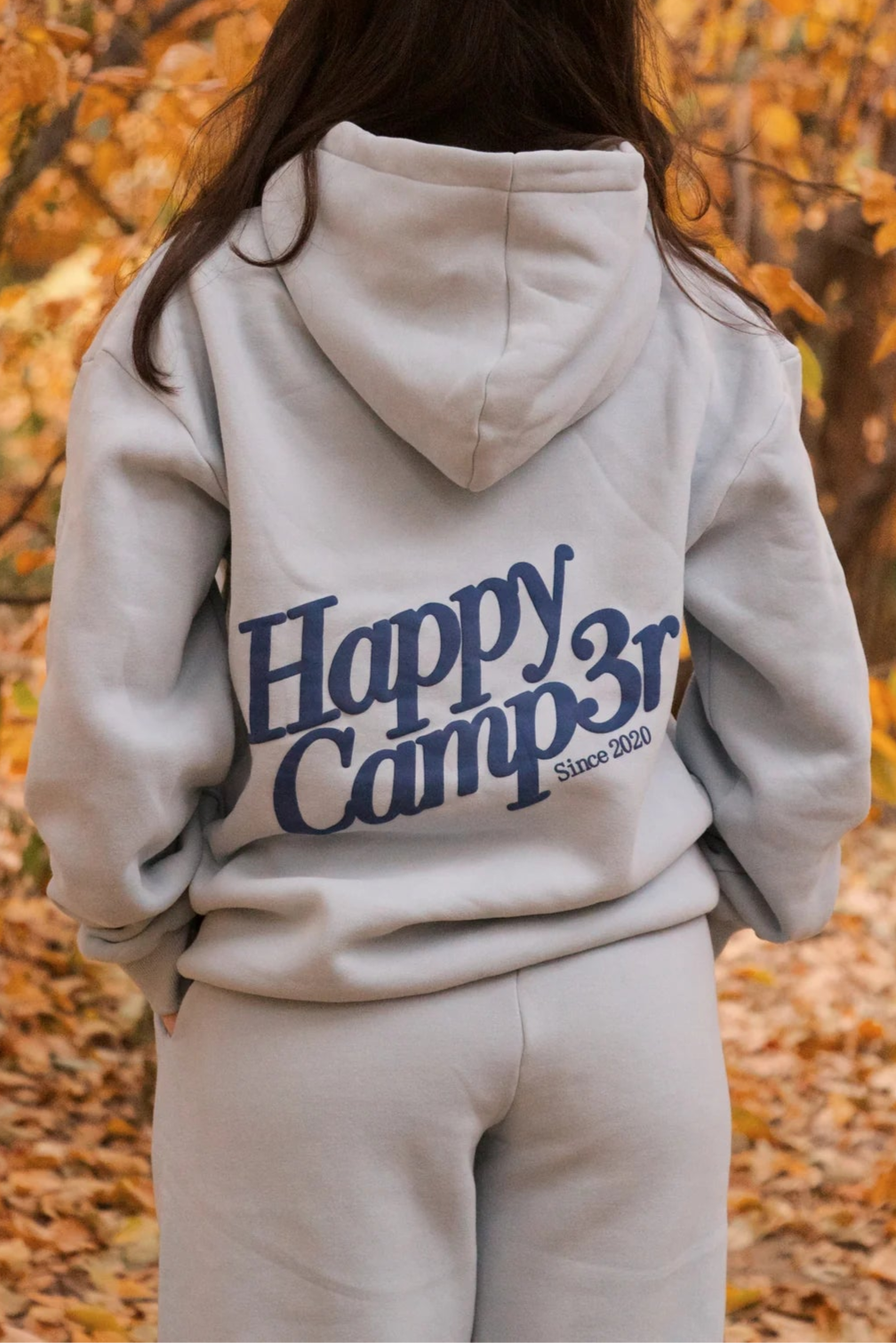 Person wearing a 'Happy Camper' hoodie in an autumn setting