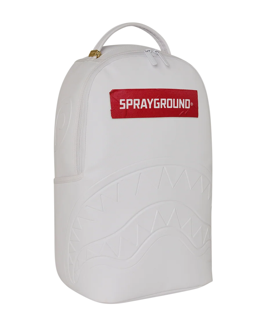 A white Sprayground backpack featuring an embossed shark mouth pattern on the front and a red rectangular logo patch with white text at the top, shown against a plain white background.