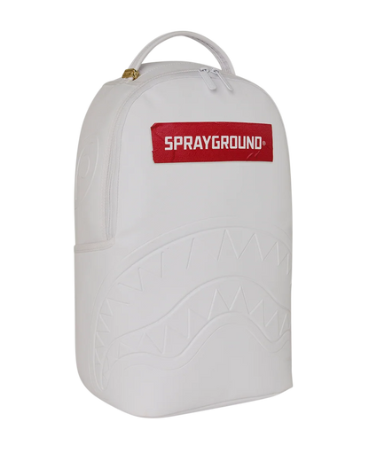 A white Sprayground backpack featuring an embossed shark mouth pattern on the front and a red rectangular logo patch with white text at the top, shown against a plain white background.