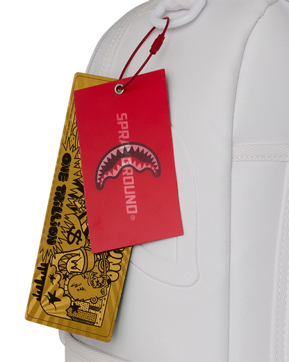 A close-up of a white garment with a red and yellow hanging tag. The red tag has the text 'SPRAYGROUND' and a shark-mouth graphic, while the yellow tag has black graffiti-style artwork and text.
