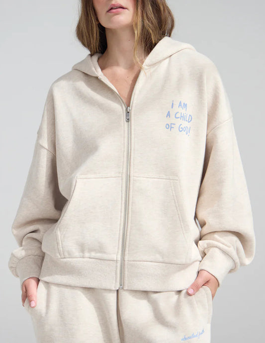 Woman wearing a beige hoodie with text on it against a plain background
