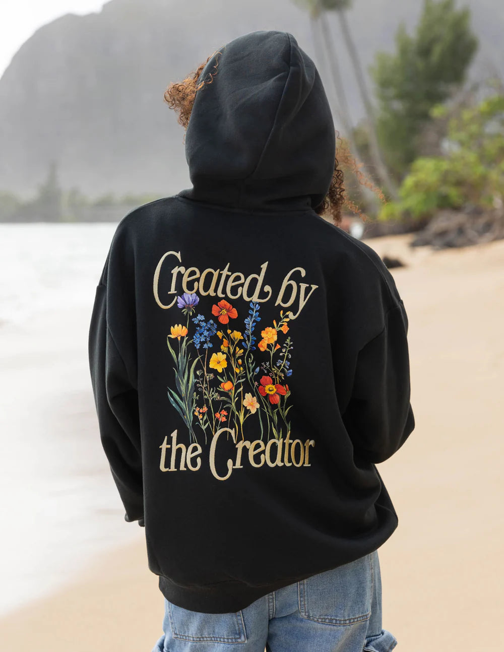 Person wearing a black hoodie with floral design and text on the back, standing outdoors.