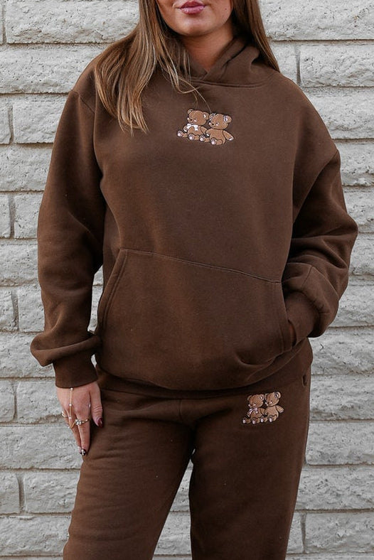 Person wearing a brown tracksuit standing against a gray brick wall.