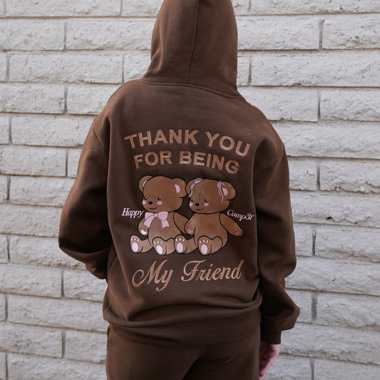 Brown hoodie with teddy bears and text on the back against a brick wall.