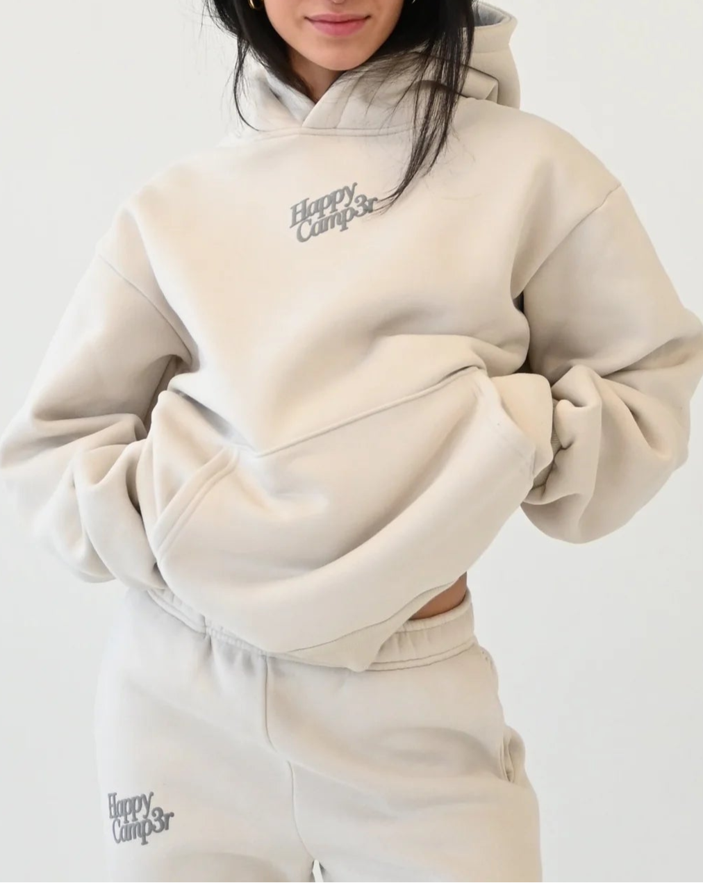 Person wearing a beige hoodie and pants with 'Happy Camper' text on a white background