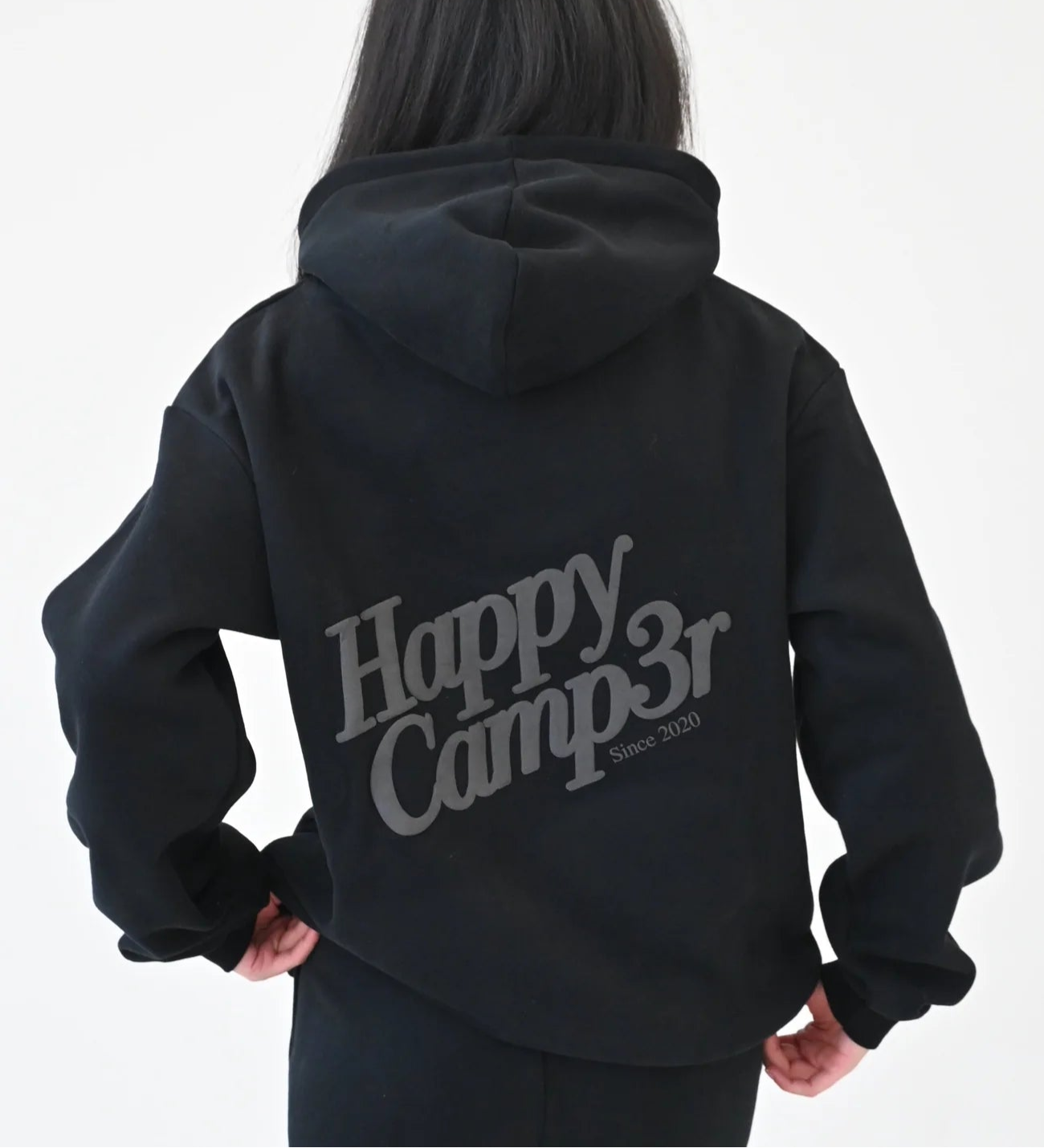 Person wearing a black hoodie with 'Happy Camp3r' text on the back against a white background
