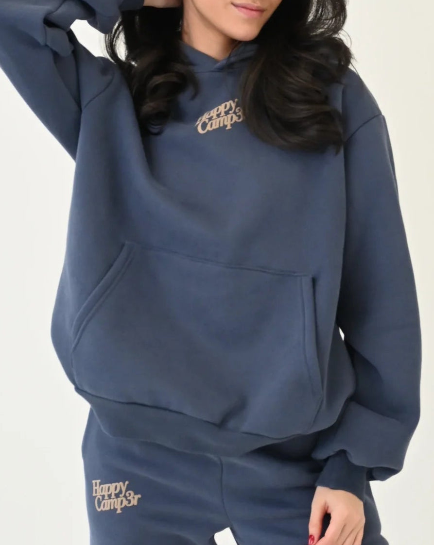 Woman wearing a blue hoodie and pants with 'Happy Campers' branding on a white background 