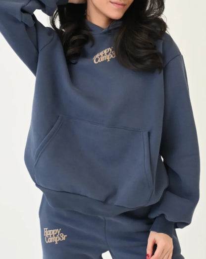 Woman wearing a blue hoodie and pants with 'Happy Campers' branding on a white background 