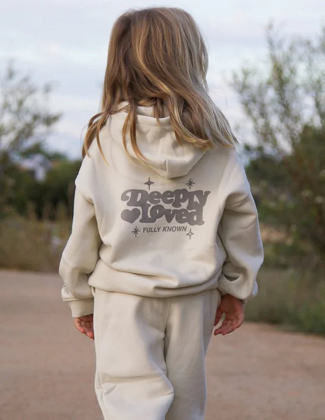 Child wearing a beige hoodie and pants walking on a dirt path with trees in the background