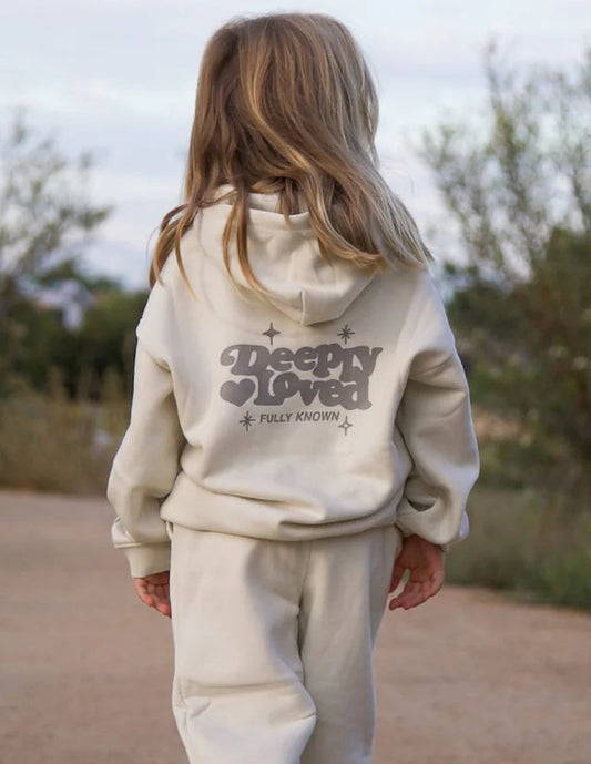 Child wearing a beige hoodie and pants walking on a dirt path with trees in the background