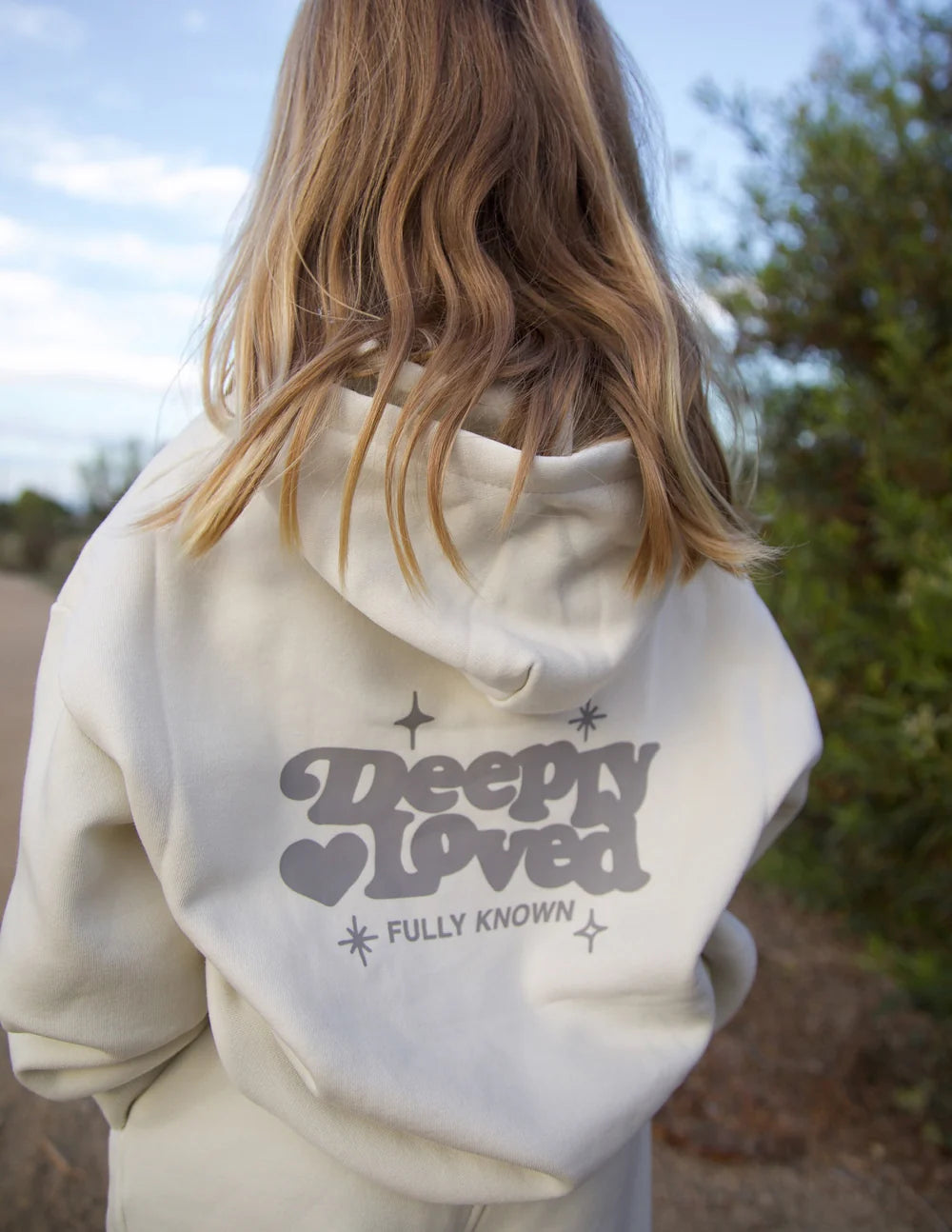 Person wearing a white hoodie with 'Deeply Loved' text outdoors