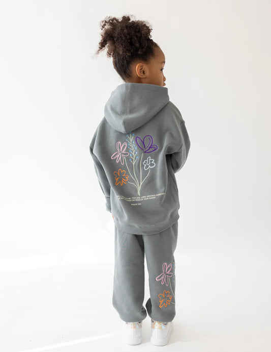 Child wearing a gray hoodie and pants with floral designs on a white background