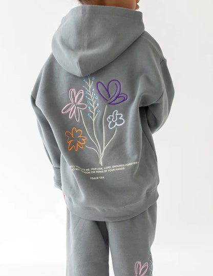 Child wearing a gray hoodie and pants with floral designs on a white background