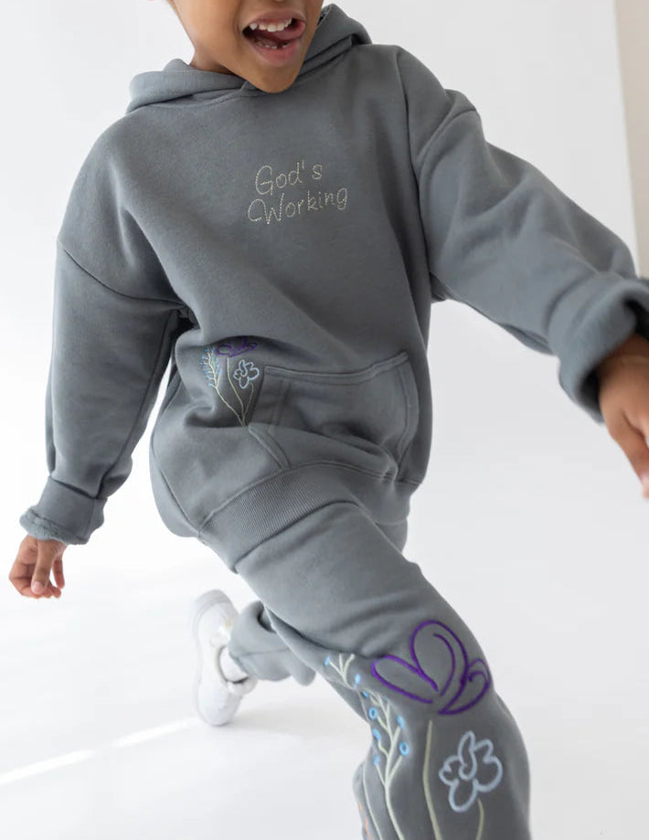 Child wearing a gray hoodie and pants with floral designs on a white background