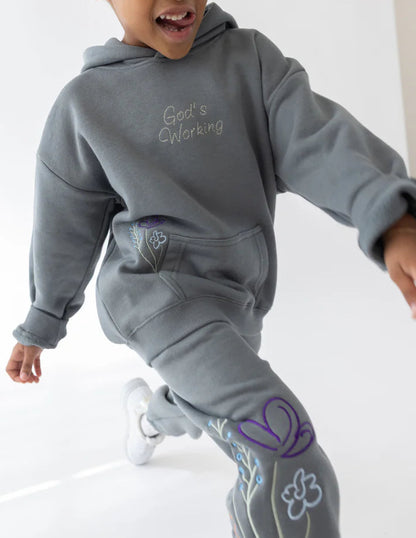 Child wearing a gray hoodie and pants with floral designs on a white background