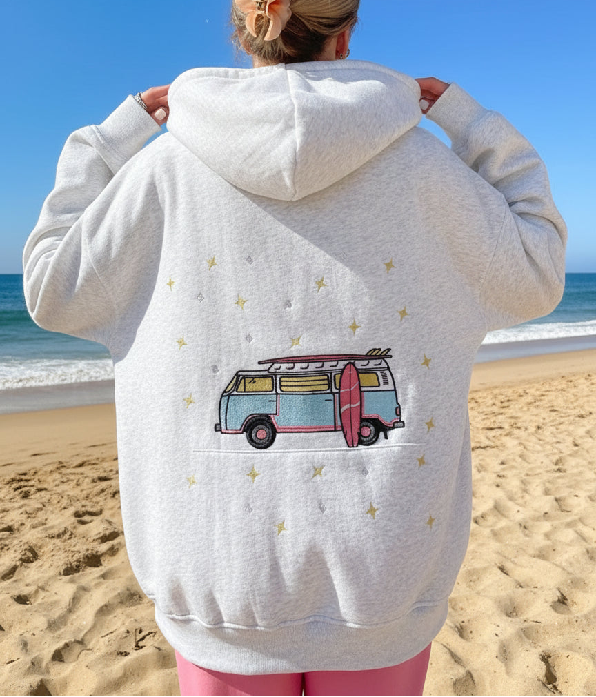 Person wearing a light gray hoodie with a van design on the back, standing in a bedroom.