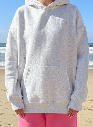 Person wearing a gray hoodie with small yellow stars on a beach